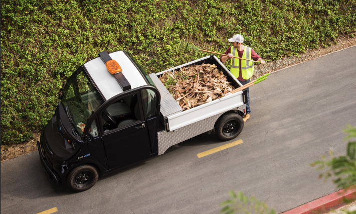 A man loading leaves and branches into the truck bed of an electric vehicle in the park