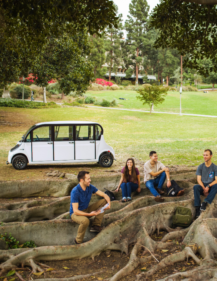 People relaxing next to an electric shuttle vehicle in the park