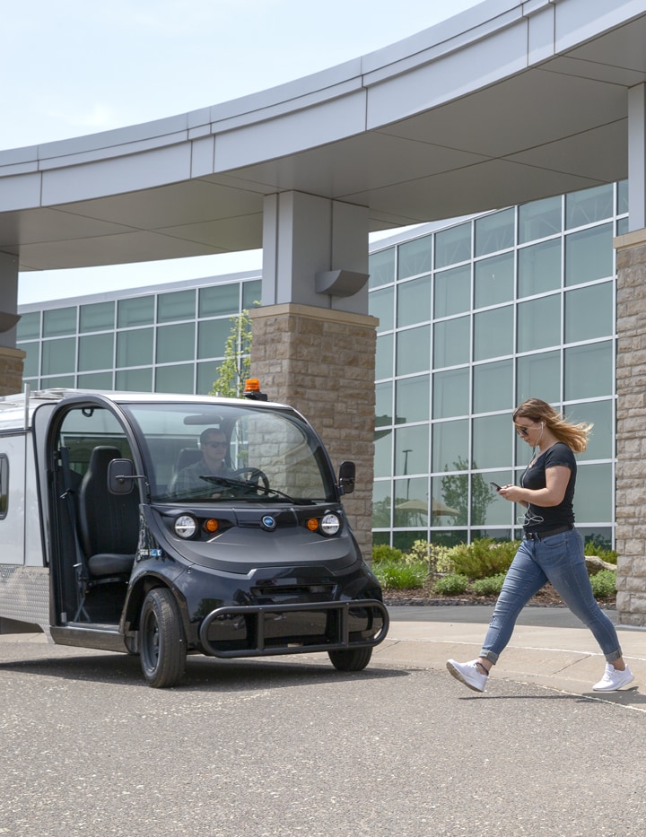 A woman looking at her phone and walking to an electric vehicle parked outside a building