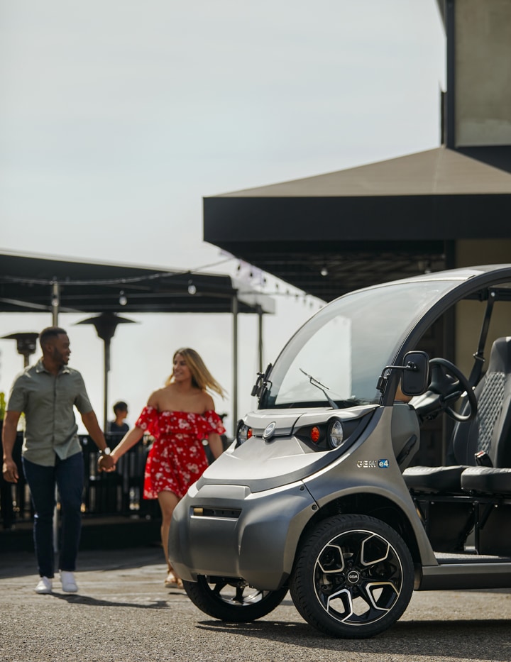 Man and a woman holding hands walking back to their GEM electric vehicle from restaurant in the background