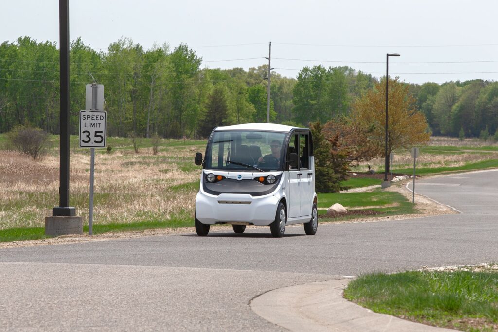 Man driving a GEM electric vehicle near a wooded area