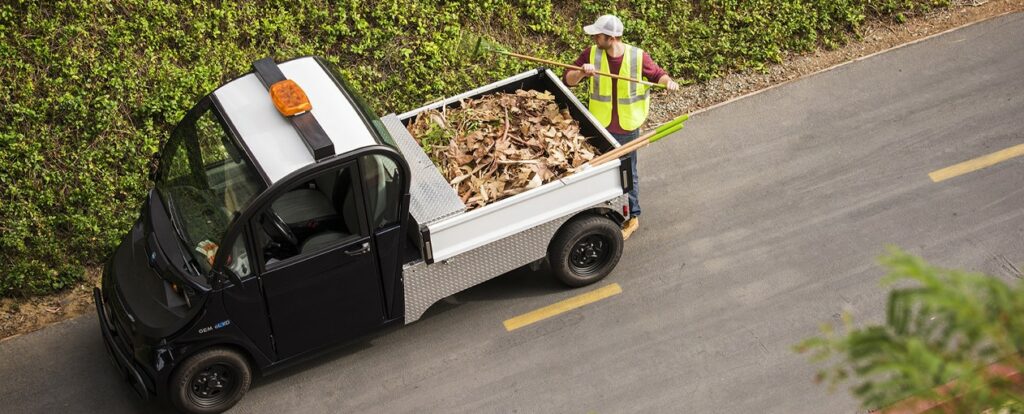 A man loading leaves and branches into an electric vehicle in the park