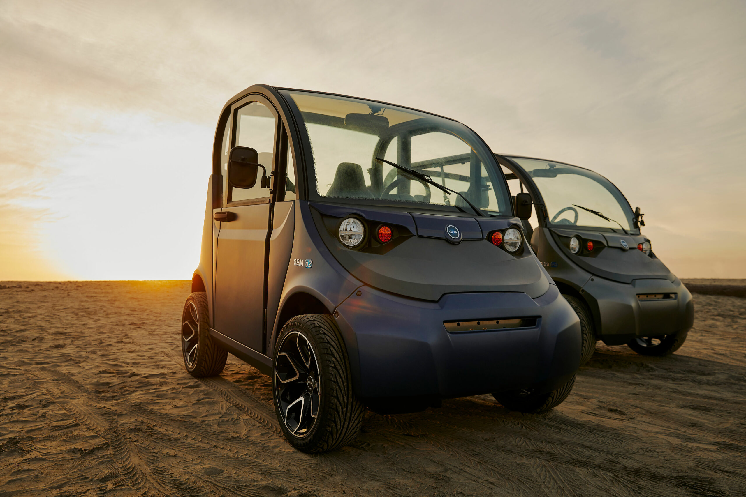 Two electric vehicles parked side by side in the sand at sunset