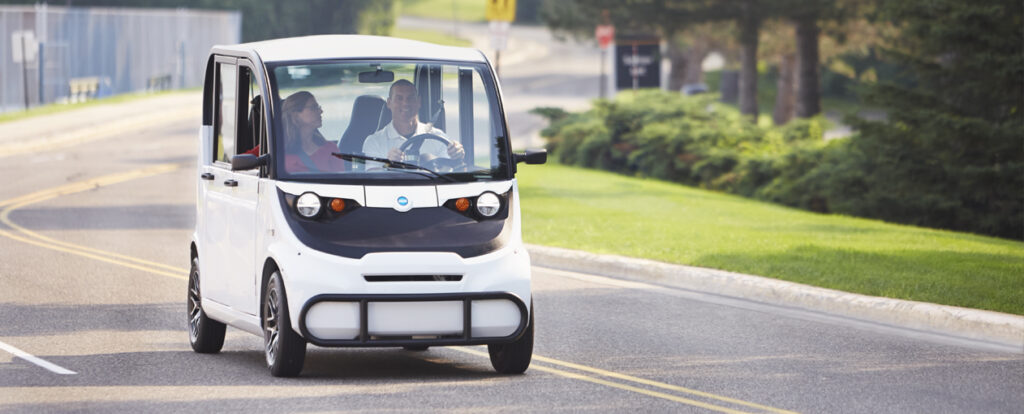 A man and a woman riding in a white electric vehicle on the street