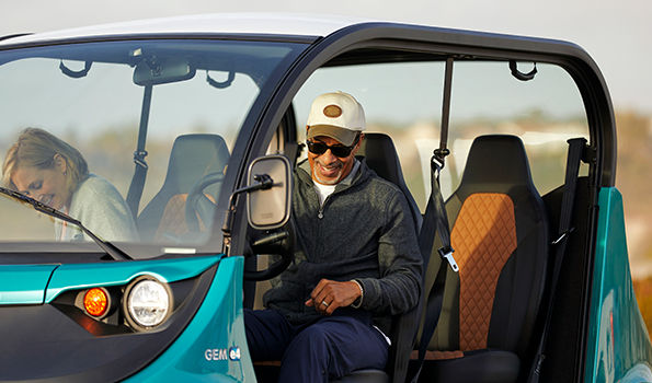 A man and a woman smiling inside a teal GEM electric vehicle