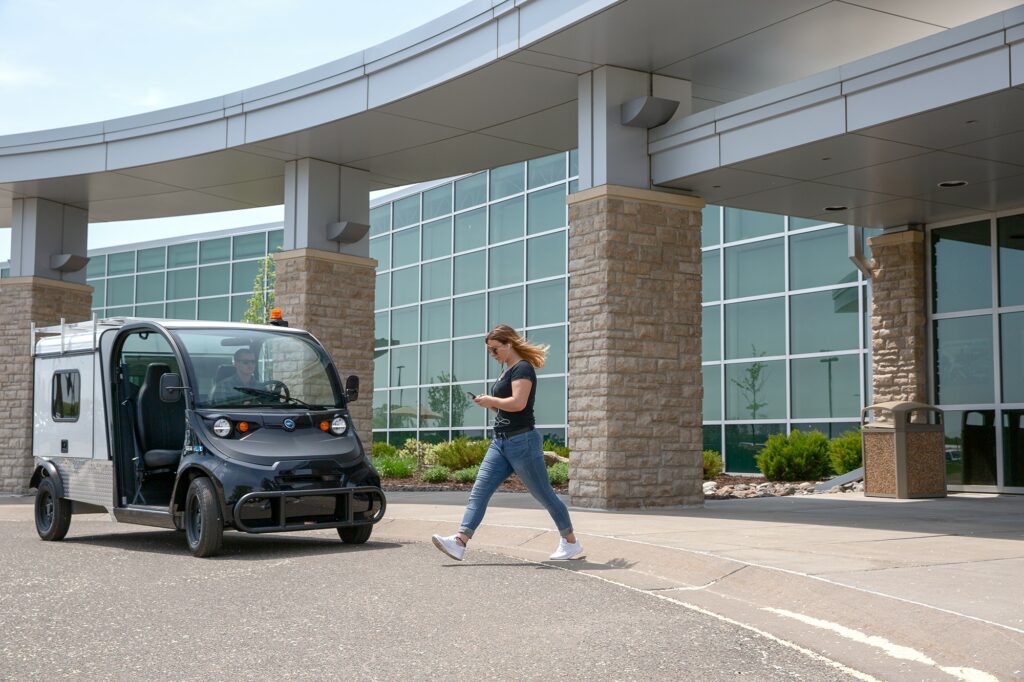 A woman looking at her phone and walking to an electric vehicle parked outside a building
